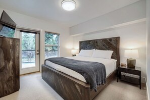 A bedroom with a large bed, a nightstand with a lamp, a wooden headboard, and a door leading to a balcony. - Modern Mountain Living, New Listing (Silverthorne)