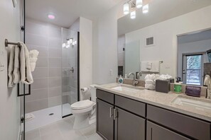 A modern bathroom with a glass shower enclosure, a toilet, a sink with a vanity, and a large mirror. - Modern Mountain Living, New Listing (Silverthorne)