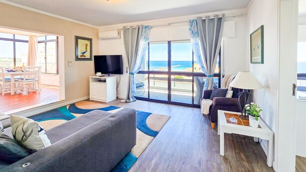 A living room with a sofa, a TV, a lamp, and a view of the sea. - Penthouse Ponta da Areia | Sea & Garage (Portimão)