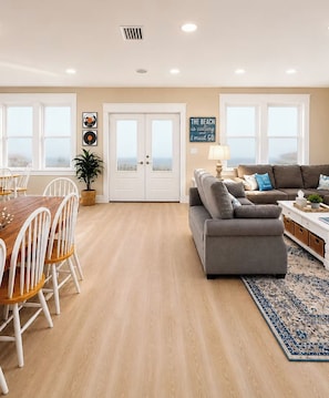 A spacious living area with a dining table, two sofas, and a large window.
