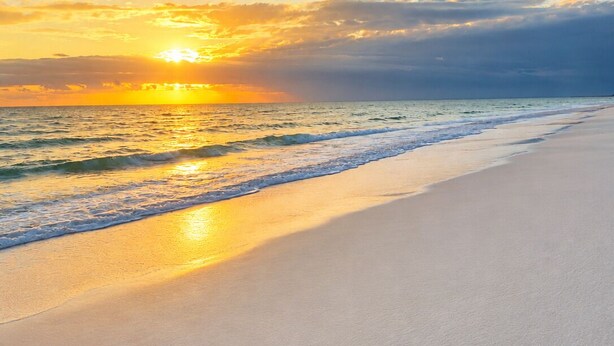 Une plage au coucher du soleil, avec un ciel dégagé et une mer calme.