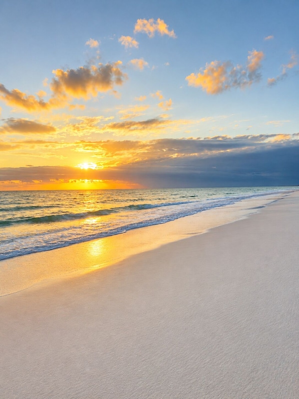 A beach with a sunset, clear sky, and calm sea.