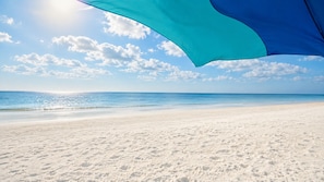 Una spiaggia con cielo sereno, una riva sabbiosa e un ombrellone blu.