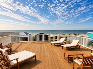 A wooden deck with lounge chairs and a view of the ocean.