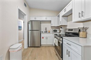 A modern kitchen with white cabinets, stainless steel appliances, and a wooden floor.