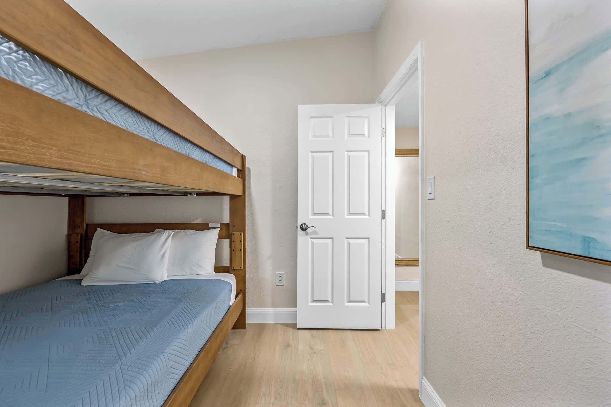 Een kamer met een stapelbed, een witte deur en een schilderij aan de muur.