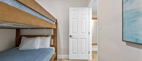A room with a bunk bed, a white door, and a painting on the wall.