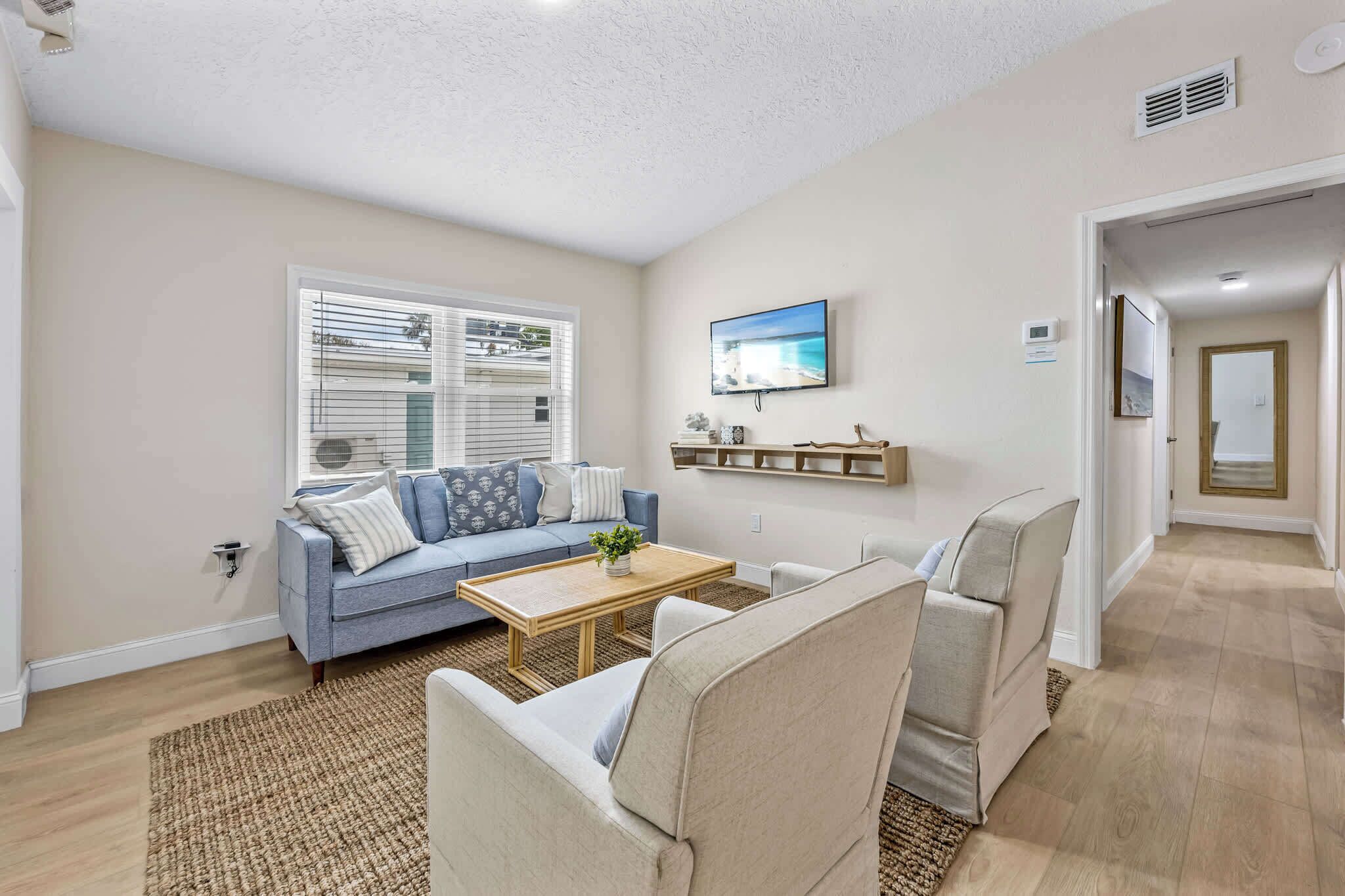 A living room with a blue sofa, beige armchairs, a wooden coffee table, and a TV mounted on the wall.
