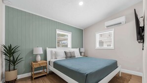 Ein Schlafzimmer mit einem Bett, zwei Nachttischen, einer Lampe, einem Topf mit Pflanze und einer Klimaanlage.