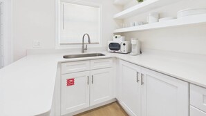 Une cuisine avec des meubles blancs, un évier en acier inoxydable, un four à micro-ondes et une machine à café.