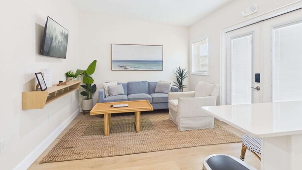Un salon avec un canapé, une table basse, un fauteuil, un téléviseur et une porte.