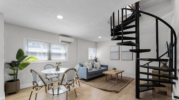 Ein modernes Wohnzimmer mit Wendeltreppe, einem Essbereich mit Korbstühlen, einer Couch und einem Couchtisch.