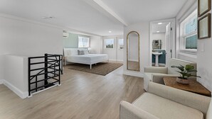 Ein geräumiges Zimmer mit Bett, einer kleinen Sitzecke, einem Spiegel und einer Küchenzeile.