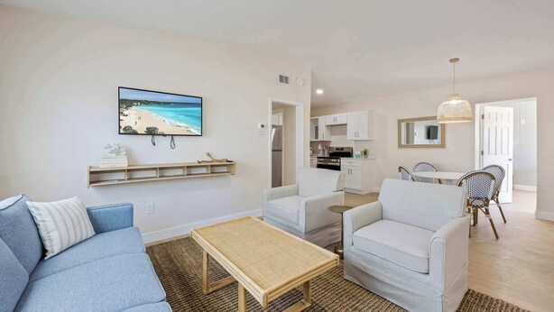 A living room with a sofa, two armchairs, a coffee table, and a kitchen area in the background. - Boardwalk Beach Bungalows Retreat (Cocoa Beach)