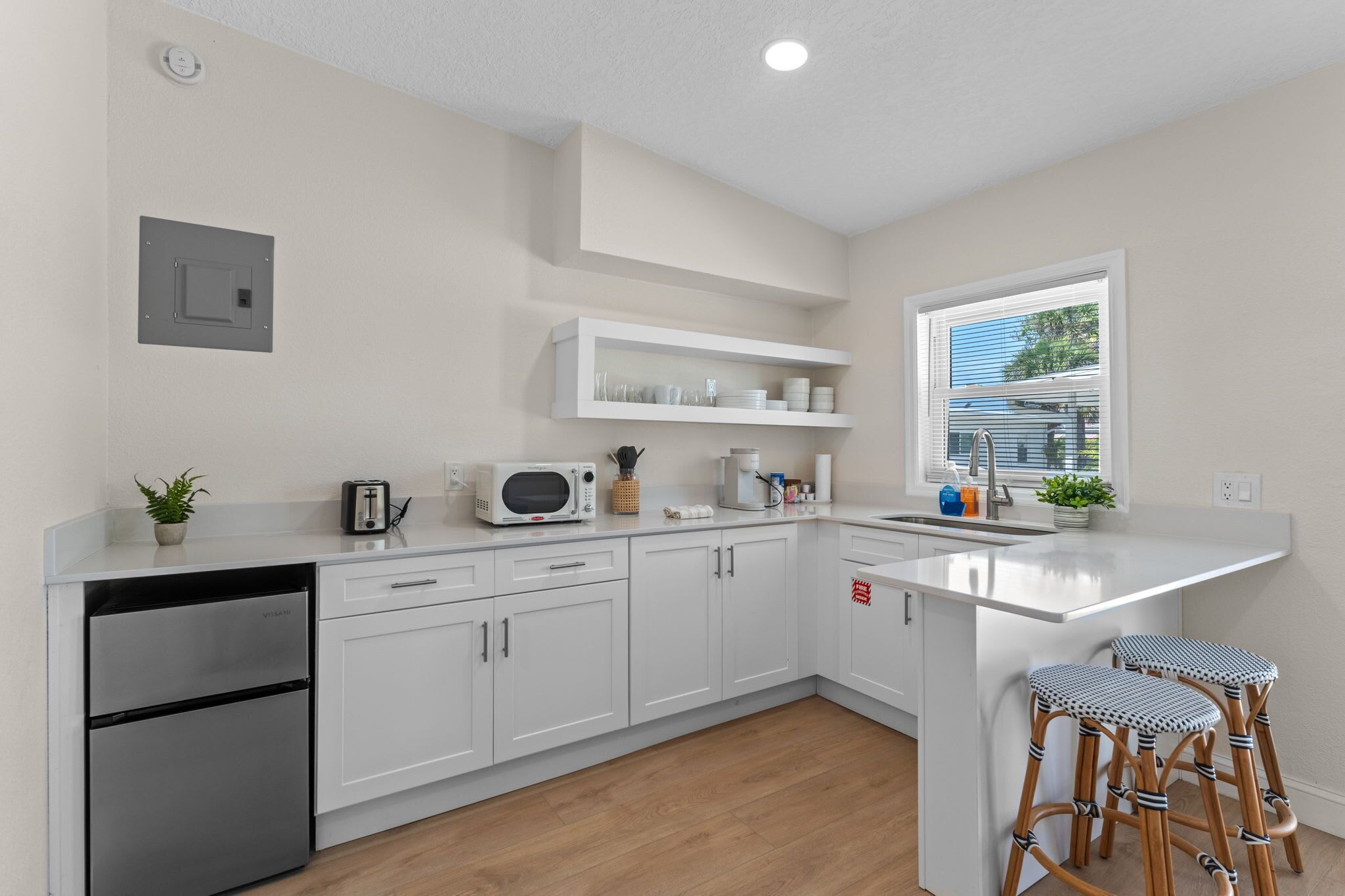 A modern kitchen with white cabinetry, a built-in microwave, a coffee maker, and a window with blinds.