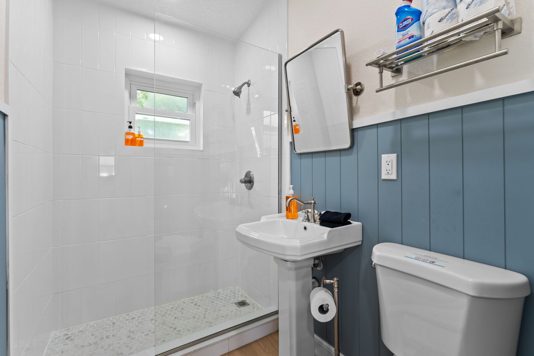 A bathroom with a shower, sink, toilet, and a window.