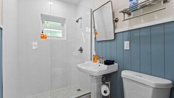 A bathroom with a shower, sink, toilet, and a window.