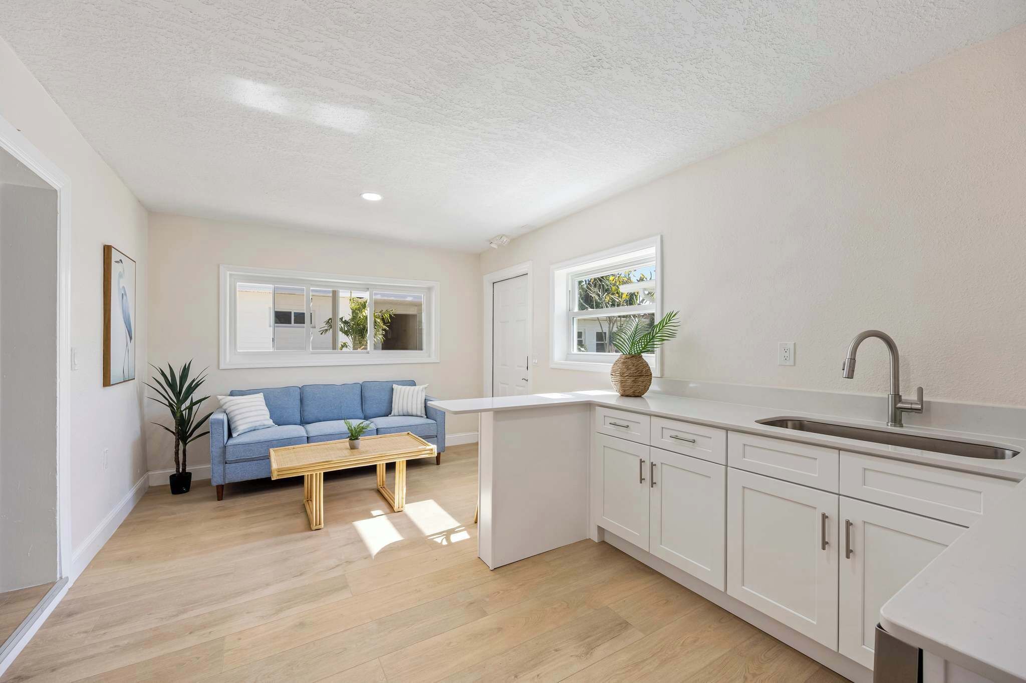 A modern kitchen with white cabinets, a blue sofa, and a wooden coffee table.