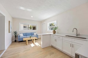 Eine moderne Küche mit weißen Schränken, einem blauen Sofa und einem Holztisch.