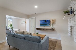 Un salon avec un canapé gris, une table basse en bois, un téléviseur fixé au mur et une cheminée.