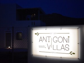 A lit signboard for 'ANTIGONI VILLAS' with 'EST. 2019' and 'LUXURY VILLAS' text, mounted on a wall. - Villa Ariadne, Divine Sea Views, Private Pool, Furnished Terrace, Andros (Andros)