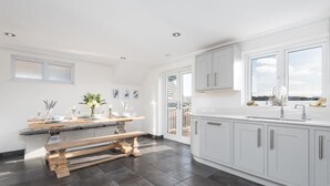 A modern kitchen with white cabinets, a wooden bench, and a large window. - Luxury Sea View House | Whitstable Beachfront (Seasalter)