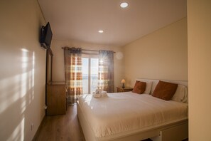 Ein Hotelzimmer mit Bett, Wand-TV, Fenster mit Vorhängen und Nachttisch mit Lampe.