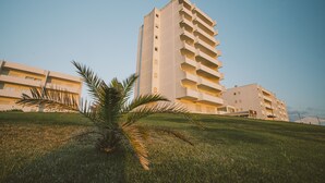 A multi-story building with balconies, surrounded by grass and a palm tree. - Best Houses 64 - Sunset Beach (Baleal)