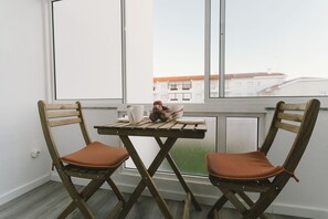 Ein Zimmer mit Fenster, zwei Holzstühle mit Kissen, ein kleiner Tisch und eine Schale mit Obst.