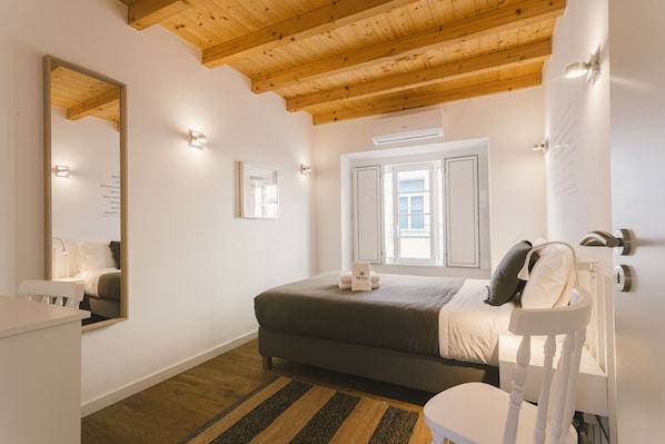Ein Schlafzimmer mit Bett, Nachttisch, Stuhl, Spiegel und Fenster.