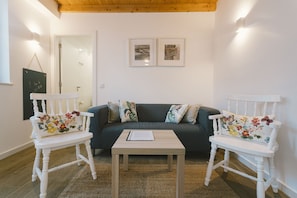 Ein Zimmer mit einem dunkelgrünen Sofa, zwei weißen Sesseln mit Blumenkissen, einem kleinen Holztisch und zwei gerahmten Bildern an der Wand.