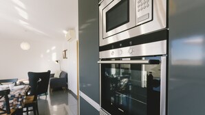Eine moderne Küche mit integriertem Backofen und Mikrowelle, ein Essbereich mit Tisch und Stühlen sowie eine Sitzecke mit einer Couch.