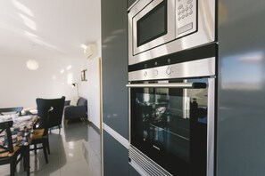 Eine moderne Küche mit integriertem Backofen und Mikrowelle, ein Essbereich mit Tisch und Stühlen sowie eine Sitzecke mit einer Couch.