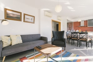 Ein Wohnzimmer mit Sofa, Sessel, Couchtisch und einem Essbereich mit Stühlen und Tisch.