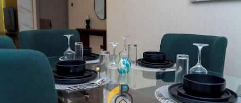 Een eettafel gedekt met zwarte borden, kommen en glazen, omringd door turquoise stoelen.
