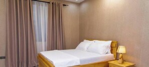 Ein Hotelzimmer mit einem Bett, Vorhängen, einem Nachttisch mit Lampe und Wandleuchte.
