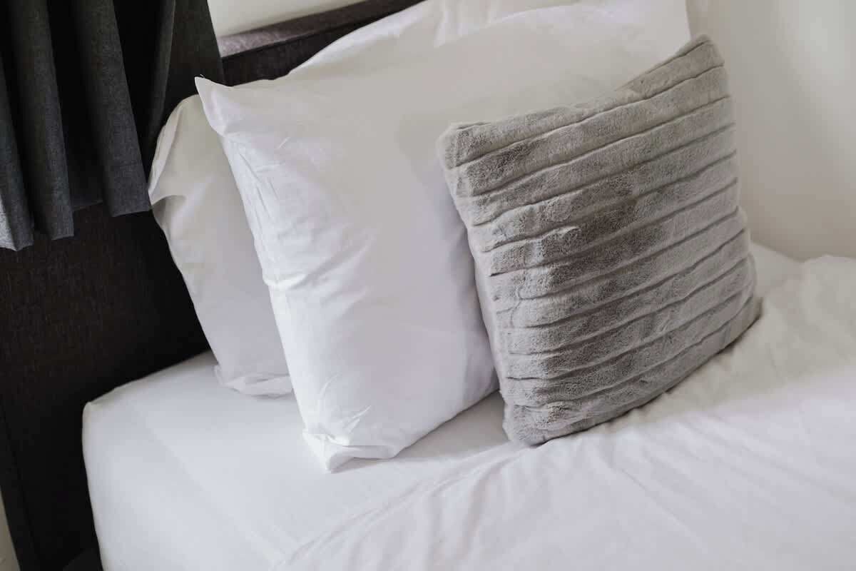 Ein Bett mit weißer Bettwäsche und einem grauen Kissen mit Struktur.