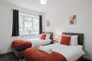 Ein Hotelzimmer mit zwei Betten, einem Fenster mit Vorhängen, einem Nachttisch mit Lampe und einem Bild an der Wand.