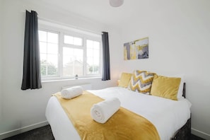 A hotel room with a bed, a window, and a painting on the wall. - Spacious 4 Bedroom Home With Free Parking (Northampton)