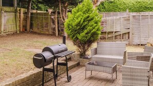 An outdoor patio with a grill, wicker furniture, and a small tree. - Spacious 4 Bedroom Home With Free Parking (Northampton)