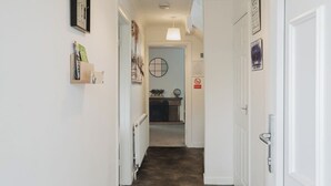 A hallway with a radiator, a door, and a wall-mounted light fixture. - Spacious 4 Bedroom Home With Free Parking (Northampton)