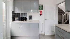 A modern kitchen with grey cabinets, a microwave, and a coffee machine. - Spacious 4 Bedroom Home With Free Parking (Northampton)