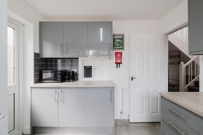 A modern kitchen with grey cabinets, a microwave, and a coffee machine. - Spacious 4 Bedroom Home With Free Parking (Northampton)