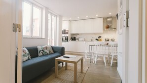 Une cuisine moderne avec des meubles blancs, un coin repas avec des chaises blanches et un salon avec un canapé et une table basse.