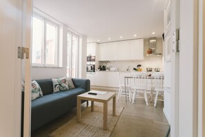 Eine moderne Küche mit weißen Schränken, ein Essbereich mit weißen Stühlen und ein Wohnzimmer mit einer Couch und einem Couchtisch.