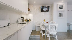 Une cuisine moderne avec des meubles blancs, un four encastré et un coin repas comprenant des chaises et une table, le tout dans des tons blancs.