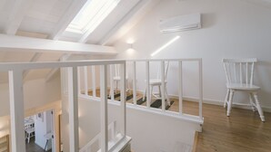 Un loft spacieux avec de hauts plafonds, une lucarne, des murs blancs et un plancher en bois.
