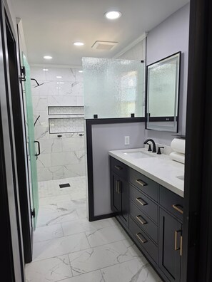 Un baño moderno con ducha, lavabo con espejo y suelo de mármol.