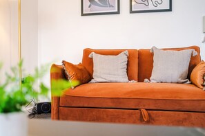 A sofa with two pillows, a plant, and a framed picture on the wall. - Stylish 2 BDR APT Free Parking Liverpool (Liverpool)