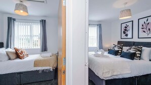Una habitación de hotel con dos camas, una ventana con cortinas, una lámpara de pared y cuadros enmarcados.